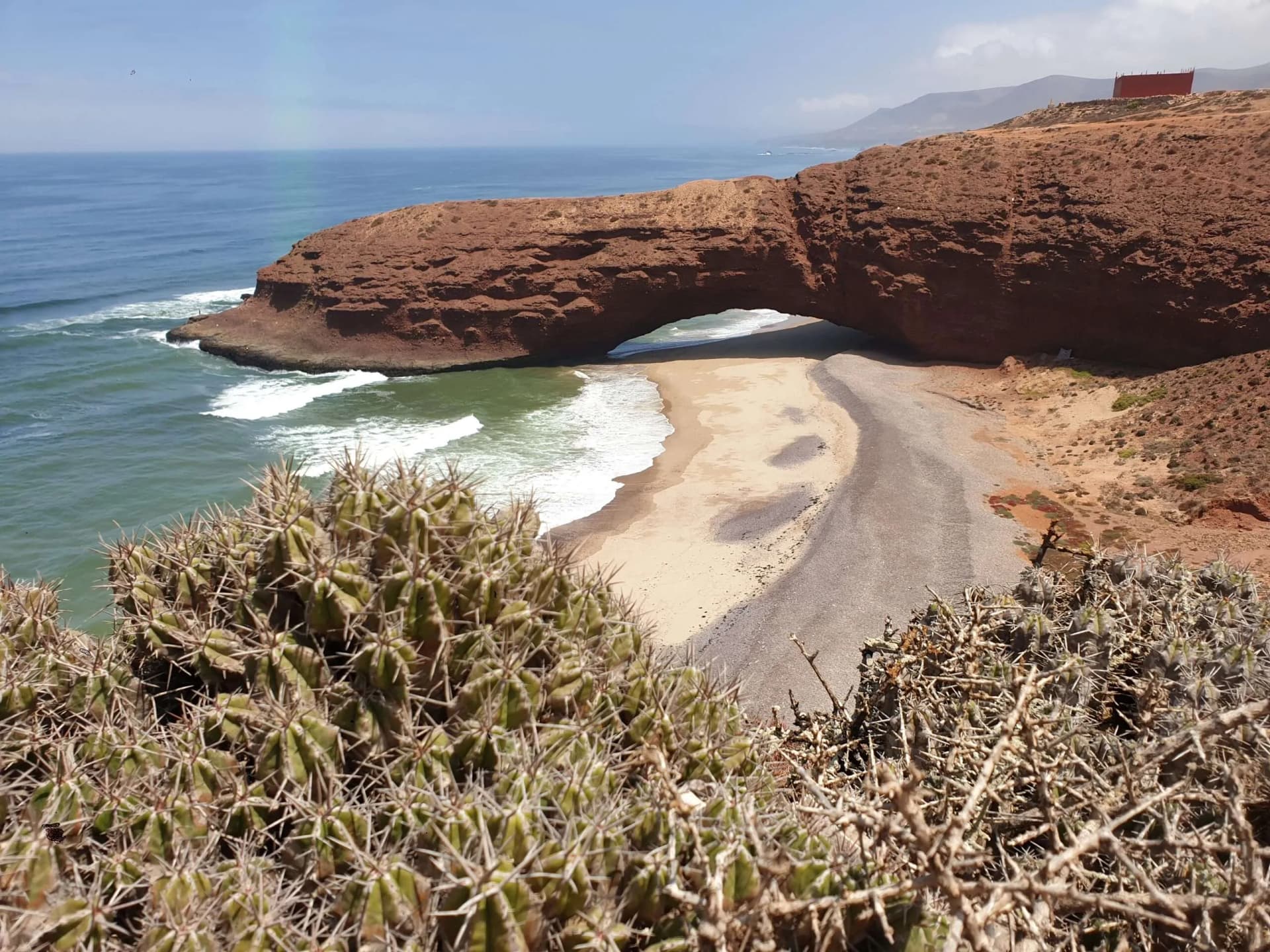 Tourists walking beneath massive natural sandstone archway at stunning Legzira beach